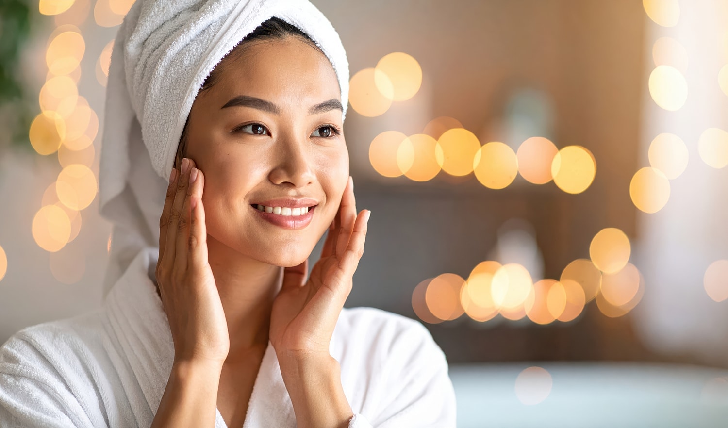 Smiling woman in robe with towel and warm lights.