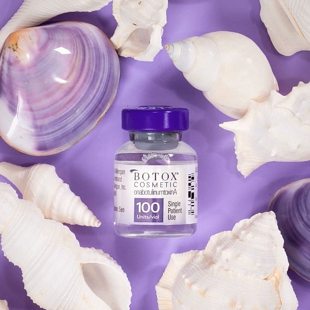 Botox vial surrounded by seashells on purple background.