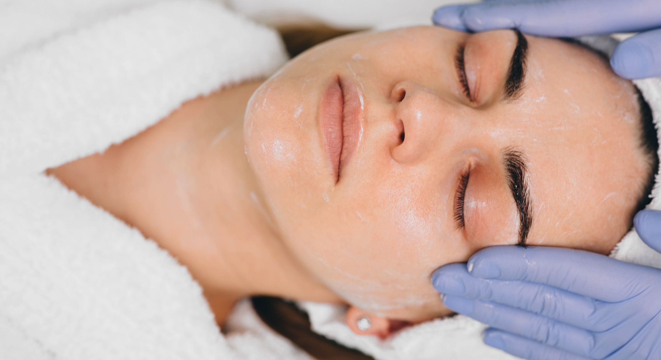 Facial treatment with gloved hands on skin.